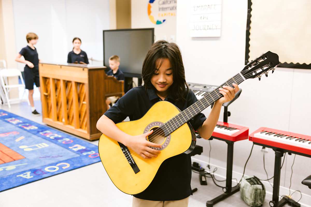 Young student concentrating while playing acoustic guitar, showcasing CIS's commitment to arts education and creative expression