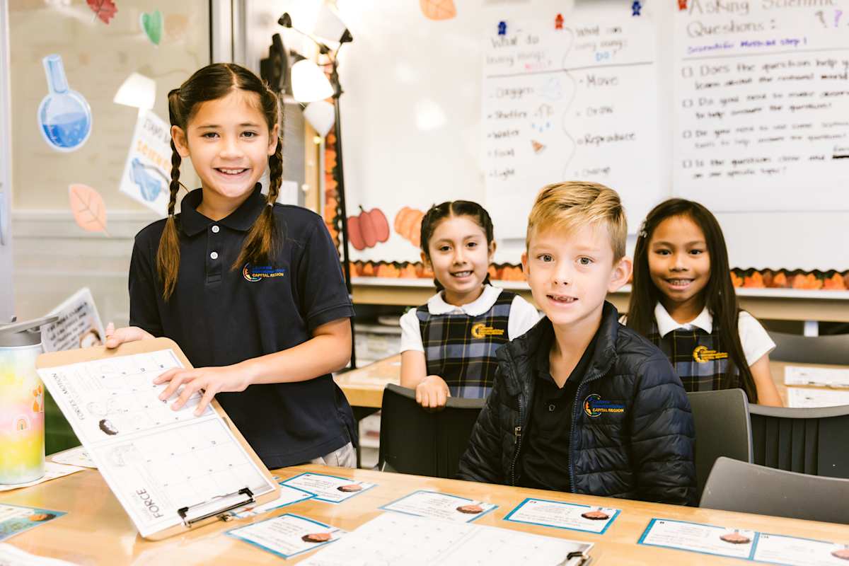 Elementary students actively participating in an interactive classroom lesson, with one student proudly displaying their work to engage with their teacher in a bright, modern learning space